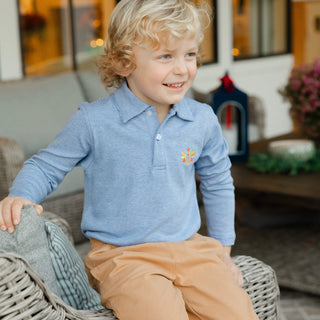 Young boy wearing Bailey Boys turkey polo shirt in royal microstripe, styled with khaki pants, sitting outdoors on wicker chair.