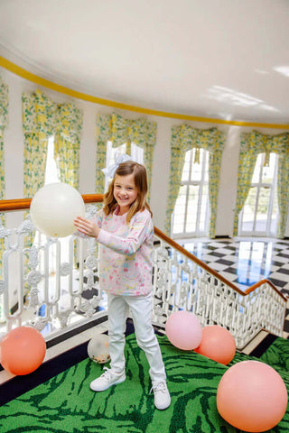 The Beaufort Bonnet Company Cassidy Ruffle Comfy Crewneck in Golden Birthday print, little girl playing with balloons in Pier Party Pink sweatshirt.