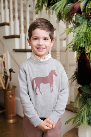 Boy in Isaac’s Horse Sweater styled with pink slacks, standing near staircase with Christmas garland—classic Southern holiday style