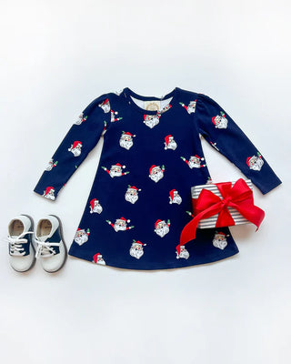 Navy long sleeve play dress with Santa Claus print, perfect for Christmas by The Beaufort Bonnet Company styled with saddle shoes and present.