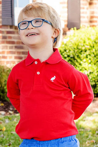 Boy smiling outdoors in red Beaufort Bonnet long sleeve polo with embroidered white stork logo on chest, styled with blue shorts.