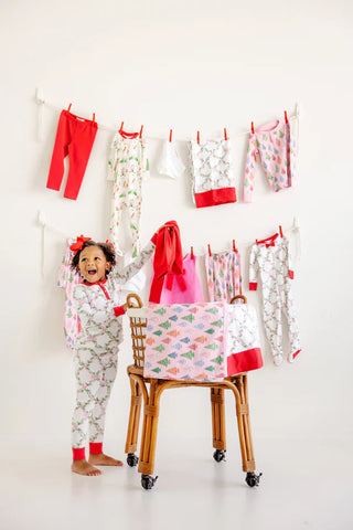 Girl wearing TBBC Sara Jane's Sweet Dreams Set with holiday holly and bow print, standing near Christmas pajamas on clothesline