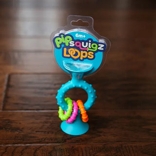 Packaged pipSquigz Loops baby toy in blue, featuring suction cup, textured handle, and colorful rattle loops, designed for ages 6 months+.
