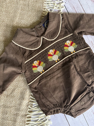 Brown baby romper with embroidered turkeys on a textured surface