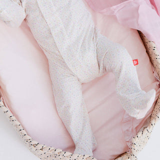 Baby wearing Magnetic Me Bedford Floral Footie with soft pastel floral pattern and footed legs while resting in a pink basket.
