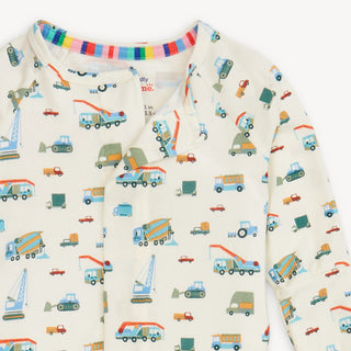 Close-up of Magnetic Me modal convertible coverall showing multicolor dump truck print and hidden magnetic closures.