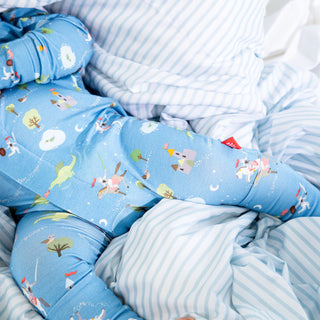 Close up of baby's legs in blue Magnetic Me Good Knight Convertible Coverall resting on blue and white striped bedding.