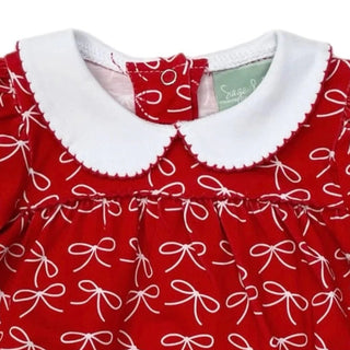 Close up of red long-sleeve baby romper by Sage & Lilly with white bow print and scalloped collar trimmed in red.