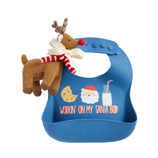 Blue silicone bib with “Workin' on my Santa bod” design and cookie, milk, Santa icons, paired with knit reindeer rattle.