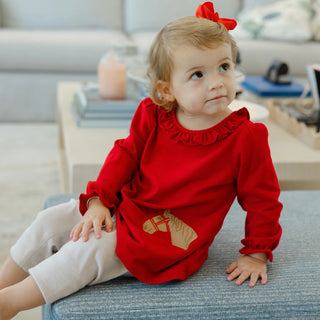 Girl sitting on sofa in Bailey Boys Pony Pals red tunic and leggings with embroidered pony detail, perfect for fall events.