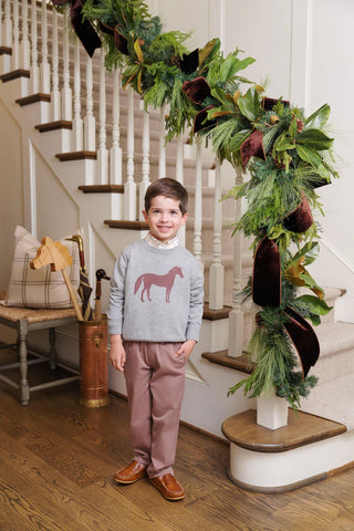 Boy wearing gray Isaac’s Intarsia Sweater with chestnut horse design, smiling indoors near holiday garland and staircase decor