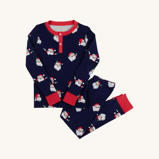 Flat lay of TBBC Sutton’s Sweet Dreams Pajamas in Jolly Old St. Nick print with Richmond Red trim featuring Santa faces on navy.