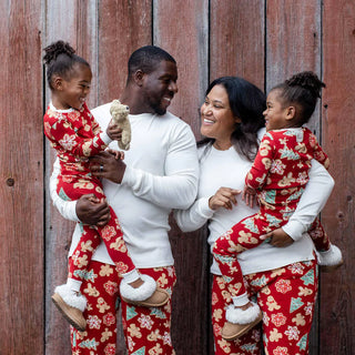 Family of four wearing matching red pajamas with gingerbread cookie designs against a wooden background.