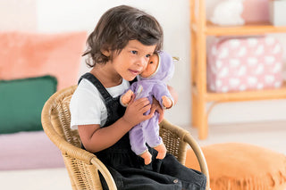 Child hugging Corolle Bebe Calin Unicorn doll dressed in purple unicorn onesie with gold horn during pretend play.