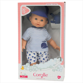 Bath Baby Marin packaged in Corolle box wearing navy striped shirt, whale shorts,  and blue hat with whale toy included.