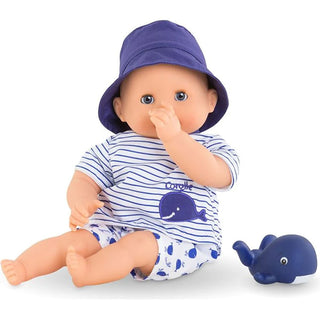 Bath Baby Marin doll sitting up in navy striped outfit with whales and hat with thumb in mouth next to small blue whale toy.