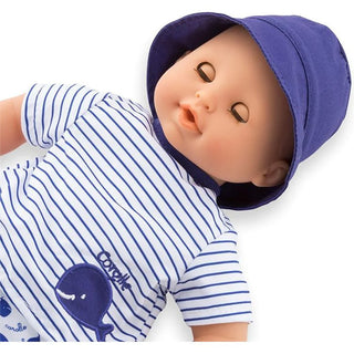 Baby doll Bath Baby Marin wearing navy striped shirt with whale applique and blue hat lying down with sleepy eyes closed.