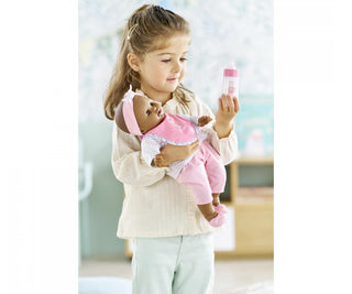 Child holding a Corolle doll wearing pink outfit while looking at a magic milk bottle accessory included in the feeding set.