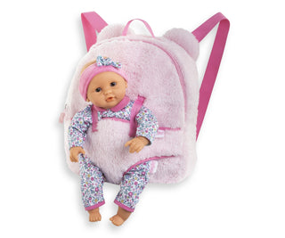 Pink plush Corolle backpack shown with 12-inch Corolle baby doll secured in front carrier, adjustable straps visible.
