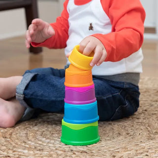 Child stacking colorful Dimpl Stack cups on the floor, pressing silicone bubbles as they build a bright tower for sensory play.