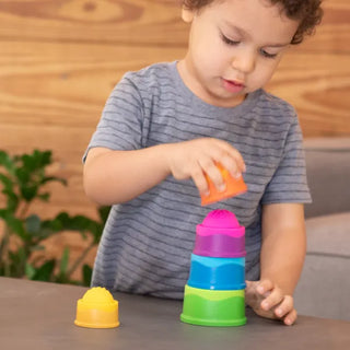 Toddler stacking vibrant Dimpl Stack cups on a table, focusing as they build a tower with sensory bubbles on top of each piece.