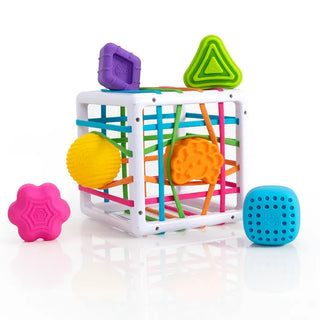 Fat Brain InnyBin toy shown with six chunky shapes including ball, flower, cube, brain, and triangle, perfect for sensory play