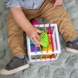Close-up of baby pushing green triangle through Fat Brain InnyBin elastic bands, exploring textures and shapes during play