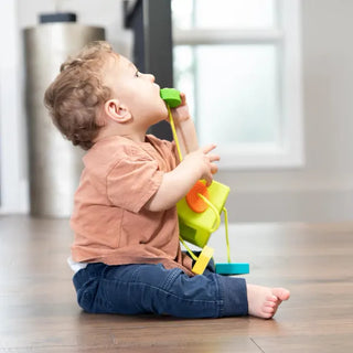 Toddler exploring OombeeCube by mouthing a tethered silicone shape, highlighting safe BPA-free design for teething and sensory play.