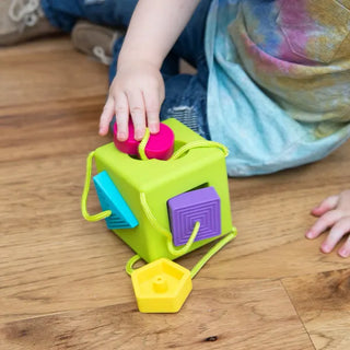 Child placing bright silicone shape into OombeeCube slot, practicing coordination and shape recognition during playtime.