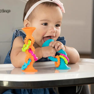 Smiling baby chewing pipSquigz Loops teether toy at highchair, enjoying silicone textures, suction base, and colorful sensory rattle rings.