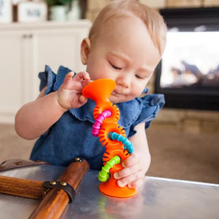 Infant exploring orange pipSquigz Loops suction toy with bendable silicone and rattle rings, designed for teething and hands-on discovery.