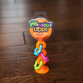Orange pipSquigz Loops baby toy with suction base and colorful textured rings, designed for teething, gripping, and sensory play.
