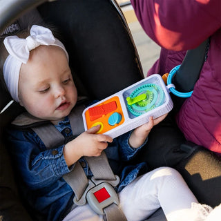 Baby plays with PlayTab Go sensory board attached to stroller, showing toddler engagement with textures and gears during travel.