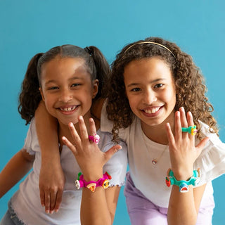 Two girls smiling and showing off their Plip Charms rings and bracelets with colorful silicone charms against a blue backdrop.