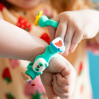 Child wears teal Plip Charms bracelet with shark, panda, and ice cream charms, twisting it playfully on their wrist.