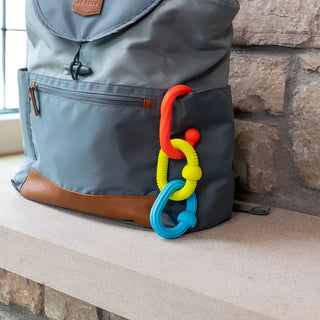 Plip Grips teether links clipped to diaper bag, ready for travel use as a teething toy or stroller sensory accessory for babies 6 months+.