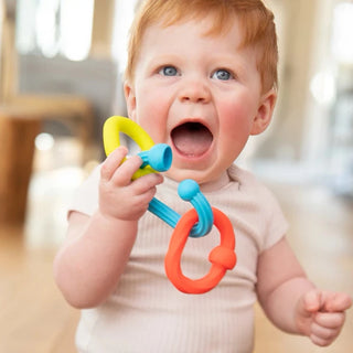 Baby smiling while holding colorful Plip Grips teether links with soft silicone textures, perfect for teething and sensory exploration.