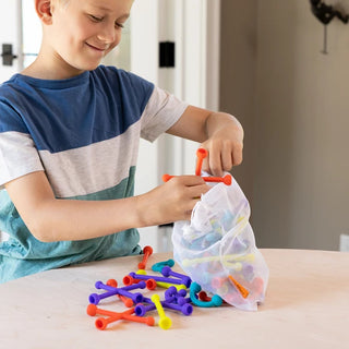 Boy empties colorful Plip Kit pieces from mesh storage bag to begin building a creative silicone structure with bendable parts.