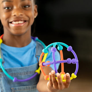 Smiling girl holds up a colorful ball-shaped Plip Kit creation made from flexible, pop-together silicone sticks and connectors.