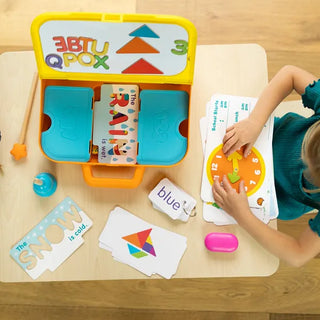 Top view of child using Pretendables School Desk with clock face, shape cards, and dry-erase boards to explore reading and time skills.