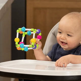 Smiling baby in high chair exploring Quubi cube with flexible elastic edges and colorful spinning beads for tactile fun and early learning play.
