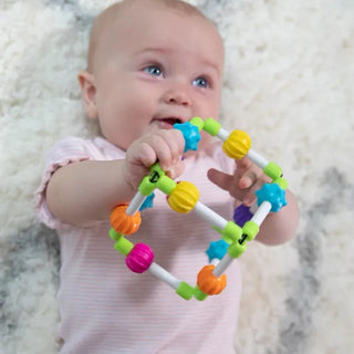 Baby lying on soft rug holding Quubi cube with colorful textured beads, bendy edges, and elastic bands for sensory play and motor skill growth.