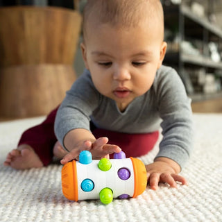 Baby crawling on floor while pushing Rolio sensory roller toy with colorful textured pegs that pop in and out for tactile exploration.
