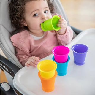 Toddler sitting in highchair chewing and playing with colorful silicone Suction Kupz stacked on tray, made for open-ended sensory fun.