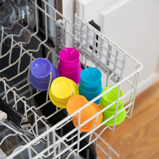 Dishwasher-safe silicone Suction Kupz in rainbow colors securely stacked inside a top-rack dishwasher for easy cleaning.