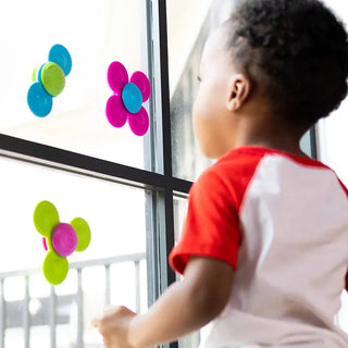 Child watching Whirly Squigz baby spinners suctioned to a window, enjoying bright silicone toys that encourage exploration and learning
