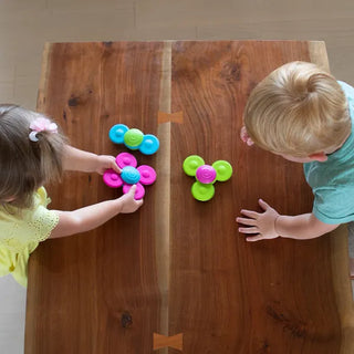Two children playing with Whirly Squigz silicone suction spinners on a wooden table, engaging in colorful, interactive sensory fun