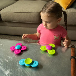 Toddler in pink shirt exploring Whirly Squigz sensory spinners on a table, designed for suction play and fine motor development