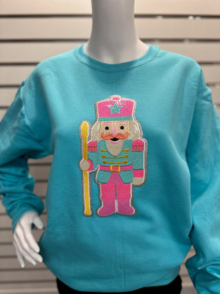 Front view of women’s aqua sequin nutcracker sweatshirt showing bright colors, detailed patch, and classic crewneck design.