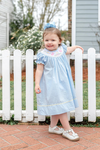 Light blue baby girl smocked dress with Easter embroidery featuring chicks, bunnies, and flowers, short puff sleeves and scalloped trim.